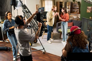 Film crew shooting scene with Caucasian actors on studio set using professional video camera equipment